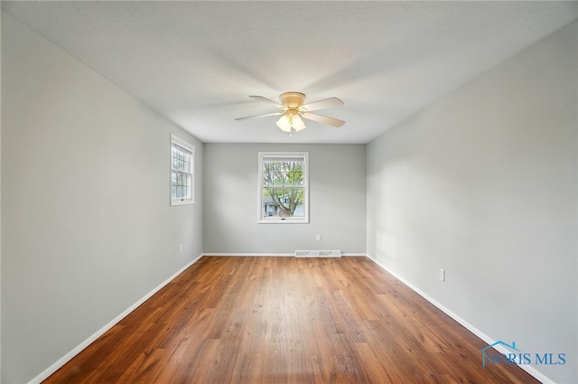 unfurnished room with baseboards, ceiling fan, wood finished floors, and visible vents