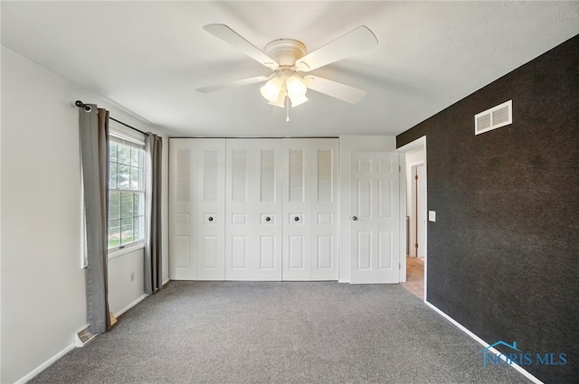 unfurnished bedroom with a closet, carpet, a ceiling fan, and visible vents