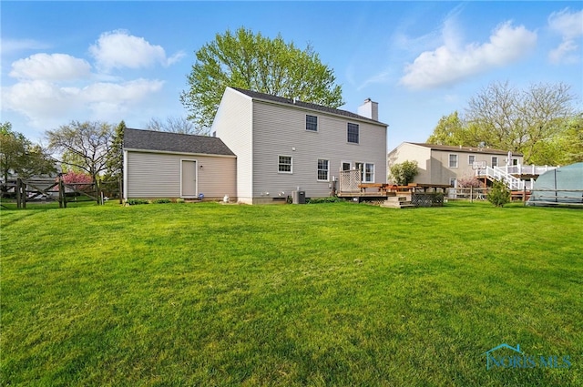 rear view of house with a lawn, fence, a chimney, and a deck