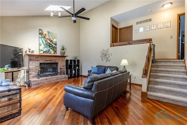 living area featuring lofted ceiling with skylight, visible vents, ceiling fan, and wood-type flooring