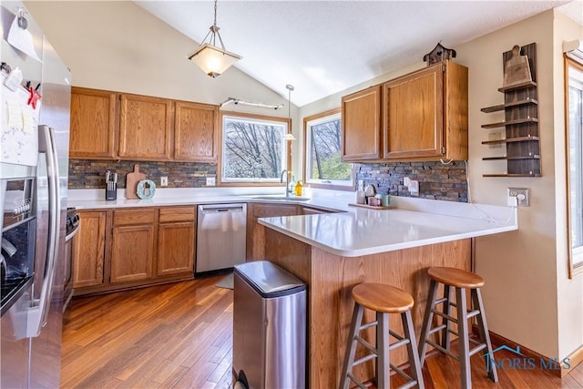 kitchen featuring a sink, brown cabinetry, a peninsula, hardwood / wood-style floors, and appliances with stainless steel finishes