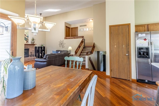 dining room with stairway, wood finished floors, visible vents, and a brick fireplace