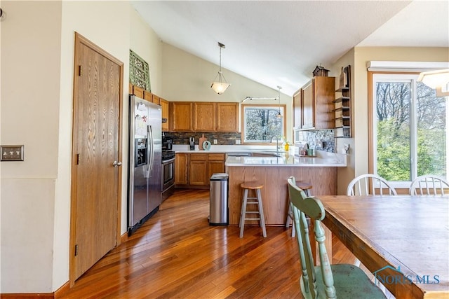 kitchen with brown cabinets, decorative backsplash, a sink, appliances with stainless steel finishes, and a peninsula