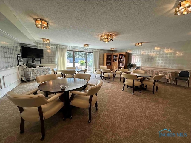 dining room with a textured ceiling, a wainscoted wall, wallpapered walls, and carpet floors