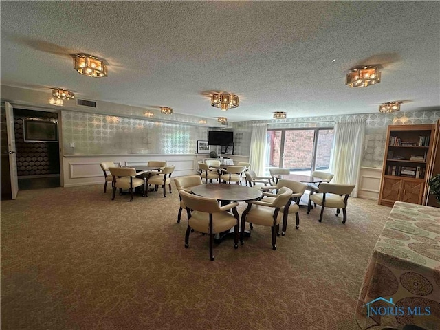 carpeted dining room featuring visible vents, wallpapered walls, and a textured ceiling