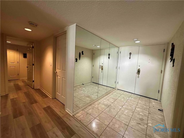 hall with recessed lighting, a textured ceiling, light wood finished floors, and baseboards