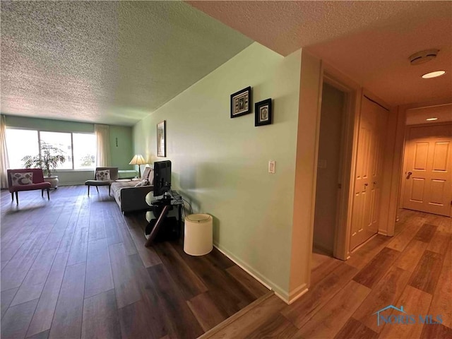 hall featuring baseboards, a textured ceiling, and wood-type flooring