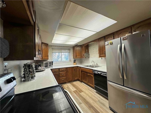kitchen featuring freestanding refrigerator, black dishwasher, light countertops, light wood finished floors, and a sink