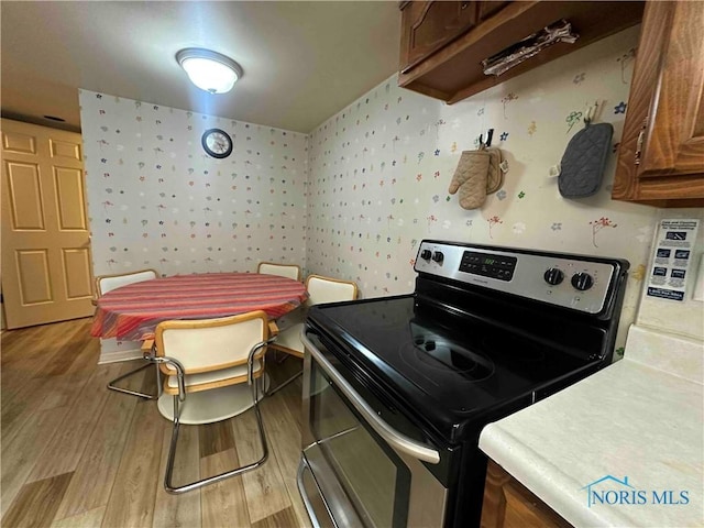 kitchen featuring stainless steel range with electric stovetop, wallpapered walls, light wood-style flooring, and light countertops