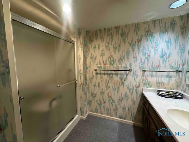 bathroom featuring a stall shower, wallpapered walls, vanity, and baseboards