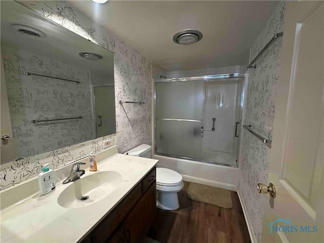 full bath with shower / bath combination with glass door, vanity, toilet, wallpapered walls, and wood finished floors