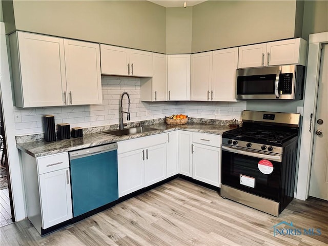 kitchen featuring tasteful backsplash, light wood-style flooring, white cabinets, a sink, and stainless steel appliances