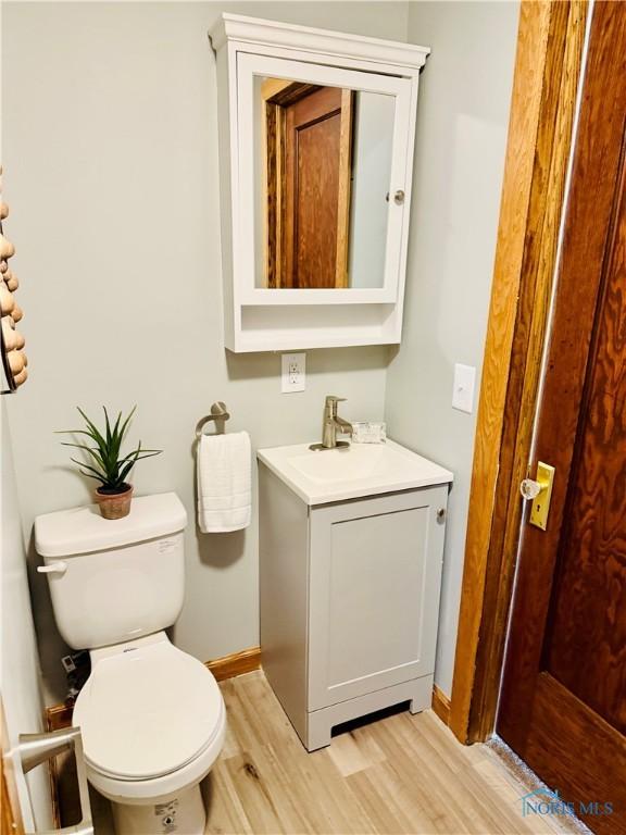 bathroom with toilet, vanity, wood finished floors, and baseboards