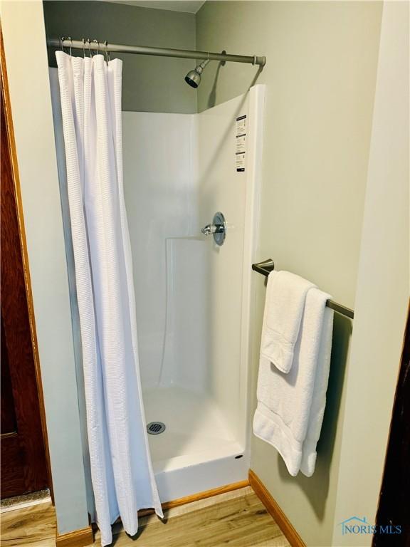 bathroom with a stall shower, wood finished floors, and baseboards