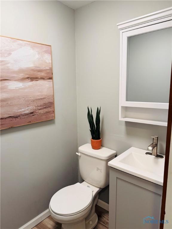 half bathroom featuring baseboards, wood finished floors, toilet, and vanity