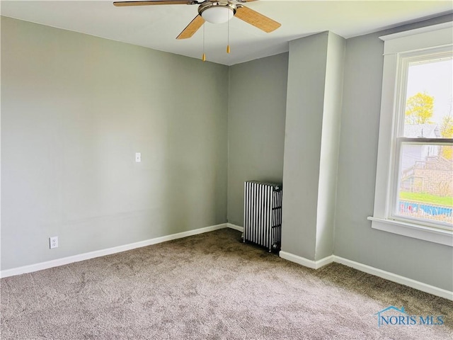 spare room with radiator heating unit, ceiling fan, a wealth of natural light, and carpet floors