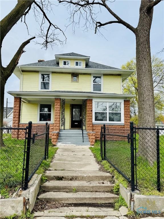 traditional style home featuring a front lawn, a fenced front yard, covered porch, and a gate