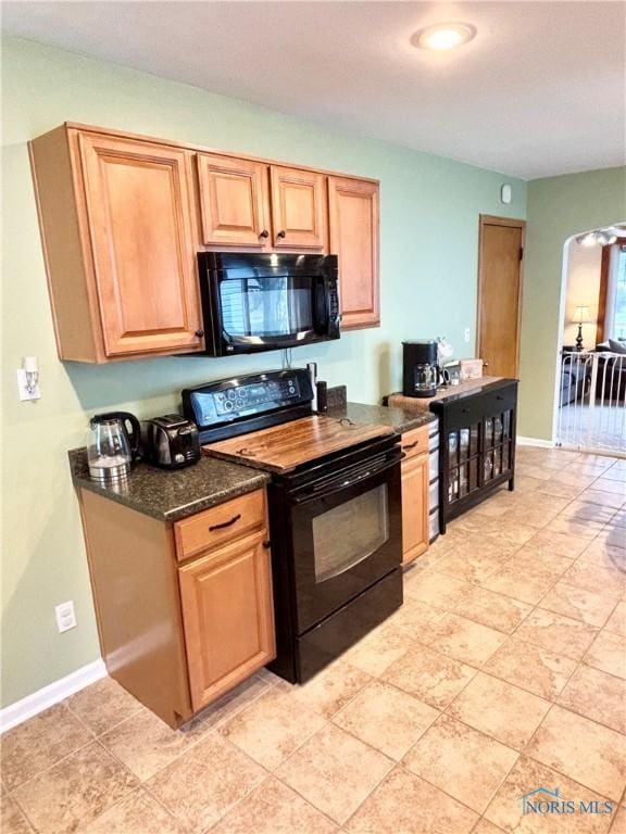 kitchen with dark stone counters, black appliances, arched walkways, and baseboards
