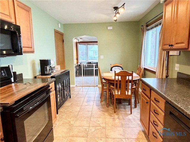 kitchen featuring black appliances, dark countertops, a healthy amount of sunlight, and arched walkways