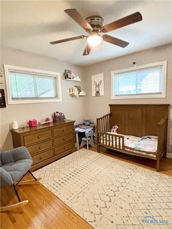 bedroom featuring a crib, wood finished floors, and multiple windows