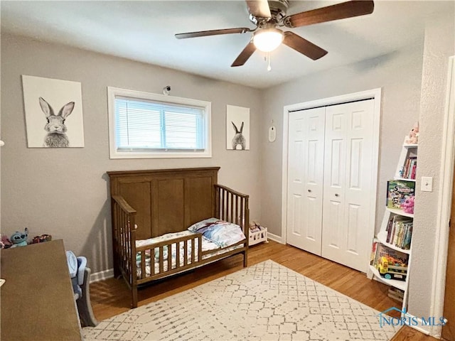 bedroom featuring wood finished floors, a nursery area, a closet, baseboards, and a ceiling fan