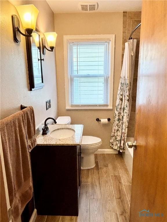 full bathroom featuring wood finished floors, shower / bath combination with curtain, toilet, vanity, and visible vents
