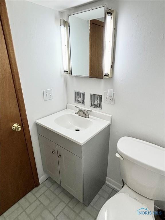 half bathroom featuring baseboards, toilet, and vanity