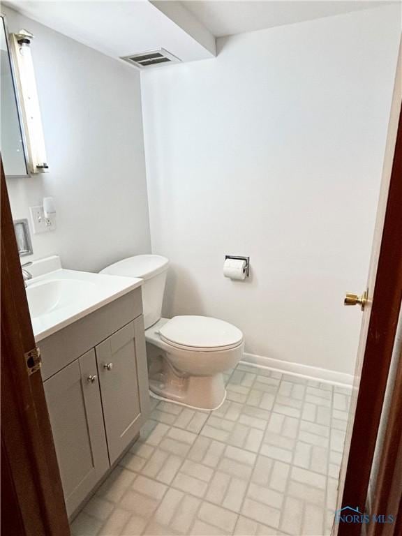 bathroom featuring vanity, brick patterned floor, toilet, visible vents, and baseboards
