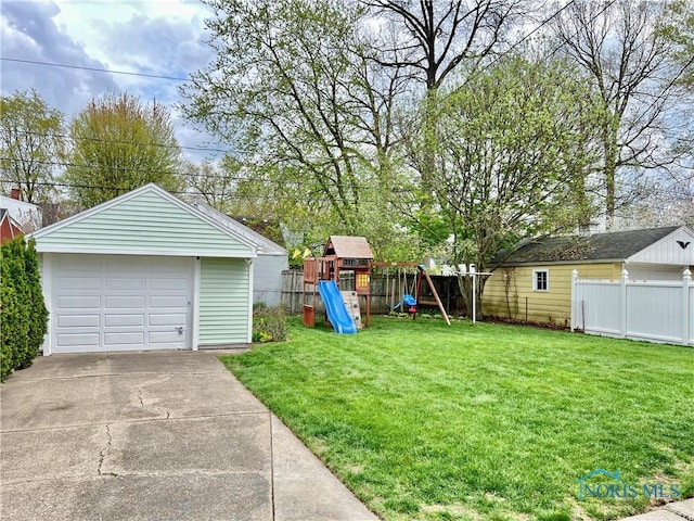view of yard with a garage, fence, an outbuilding, and a playground