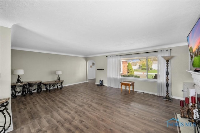 living area featuring ornamental molding, arched walkways, wood finished floors, and baseboards