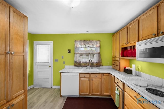 kitchen with wood finished floors, white appliances, brown cabinetry, light countertops, and a sink