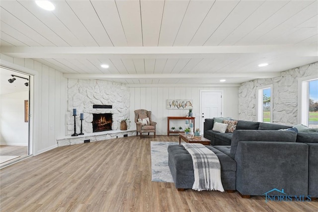 living area featuring recessed lighting, wooden ceiling, beam ceiling, a stone fireplace, and wood finished floors