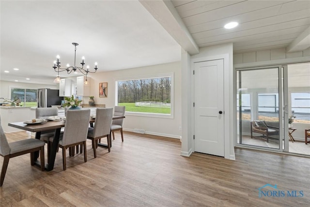 dining space featuring a healthy amount of sunlight, light wood-type flooring, and a notable chandelier