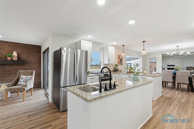 kitchen featuring a sink, freestanding refrigerator, open floor plan, a kitchen island with sink, and a peninsula
