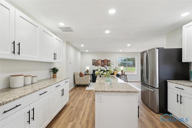 kitchen with light wood-style floors, visible vents, a kitchen island, white cabinets, and freestanding refrigerator