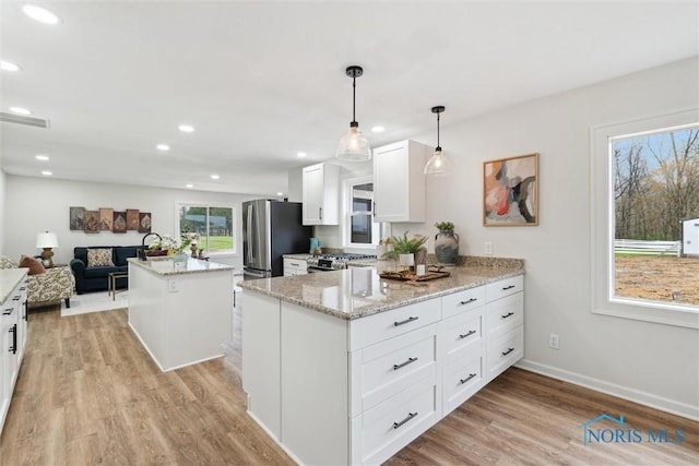 kitchen featuring light wood-type flooring, light stone counters, white cabinetry, a kitchen island, and appliances with stainless steel finishes