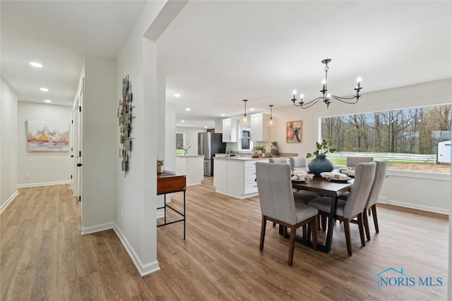 dining space with light wood finished floors, recessed lighting, an inviting chandelier, and baseboards
