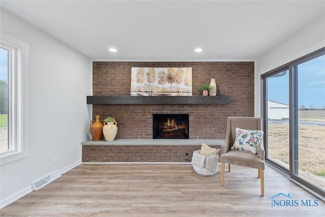 sitting room with visible vents, wood finished floors, a healthy amount of sunlight, and a brick fireplace