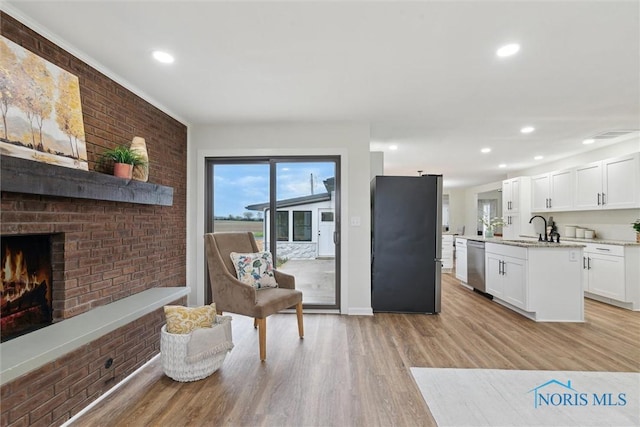 kitchen with white cabinets, a sink, light wood-style floors, stainless steel appliances, and a brick fireplace