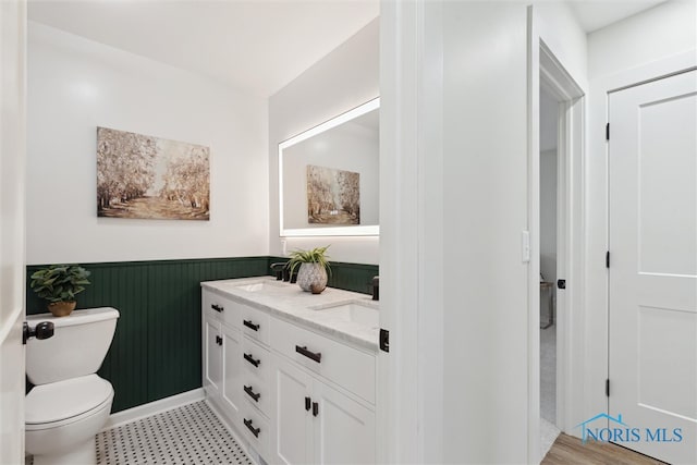 bathroom featuring tile patterned floors, a wainscoted wall, toilet, and a sink