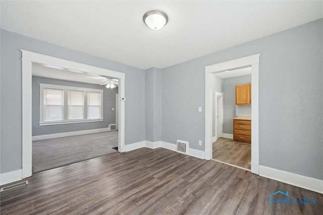 empty room featuring baseboards, visible vents, a ceiling fan, and dark wood-style flooring