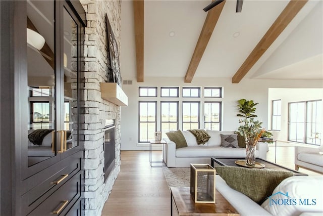 living area with visible vents, beam ceiling, light wood finished floors, high vaulted ceiling, and a stone fireplace
