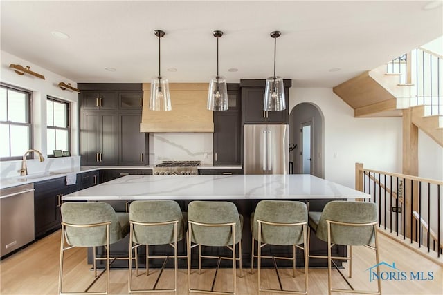 kitchen featuring appliances with stainless steel finishes, a kitchen island, wall chimney range hood, a sink, and a kitchen breakfast bar