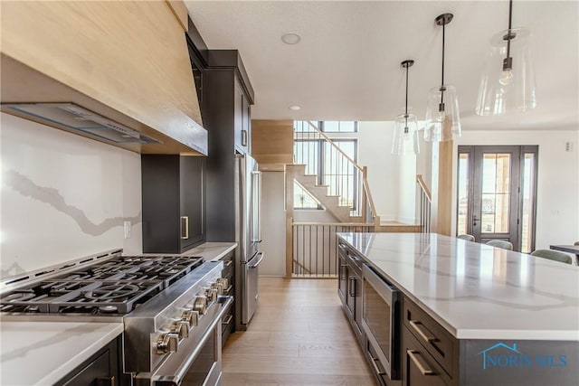 kitchen with light stone counters, stainless steel appliances, a center island, light wood-type flooring, and premium range hood