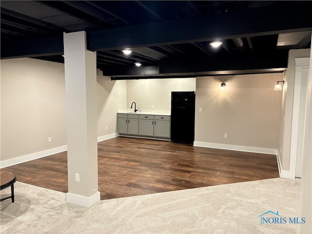 finished basement with a sink, dark wood-style floors, baseboards, freestanding refrigerator, and indoor wet bar