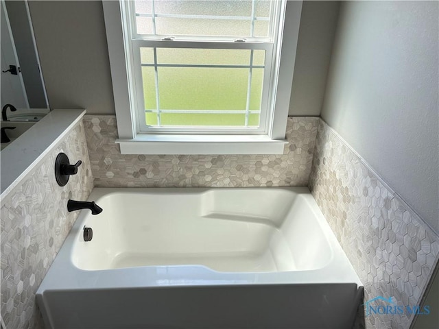 bathroom with a garden tub and a wainscoted wall