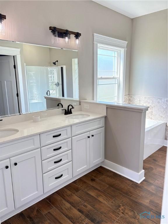 bathroom featuring a walk in shower, a garden tub, wood finished floors, and a sink