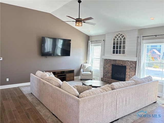 living room featuring wood finished floors, a brick fireplace, baseboards, a ceiling fan, and lofted ceiling