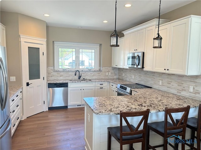 kitchen with a sink, a peninsula, white cabinets, appliances with stainless steel finishes, and dark wood finished floors