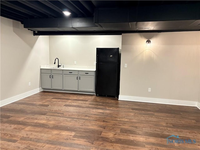 finished basement with dark wood-style flooring, a sink, freestanding refrigerator, and baseboards